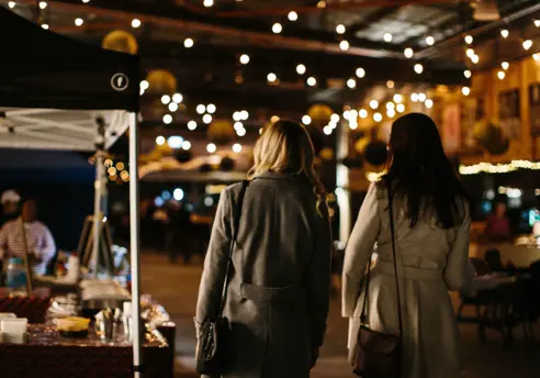 Two visitors strolling beneath string lights at the Providore Market night, Devonport