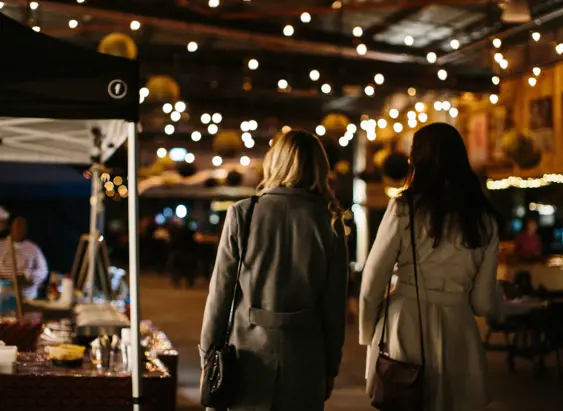 Two visitors strolling beneath string lights at the Providore Market night, Devonport
