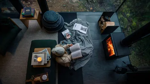 Overhead view of a person reading by a fireplace wrapped in a blanket with books and a candle at Pumphouse Point, Lake St Clair
