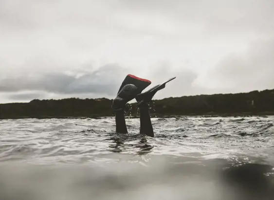 A diver's wetsuit boots and fins poke above the water surface at King Island on an overcast day