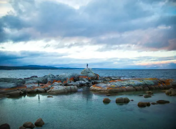 A person standing on lichen covered granite boulders at The Gulch, Binalong Bay, larapuna / Bay of Fires area