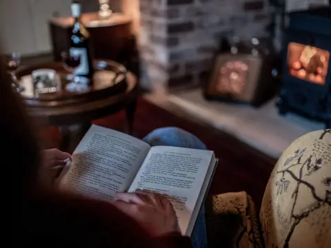 A guest reading a book by the wood fire at Old Bishop's Quarters, Fitzroy Place, Sandy Bay