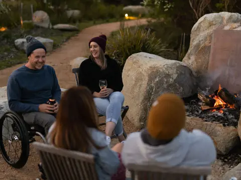 Four friends gathered around an open firepit at dusk at Little Beach Co Resort, Chain of Lagoons