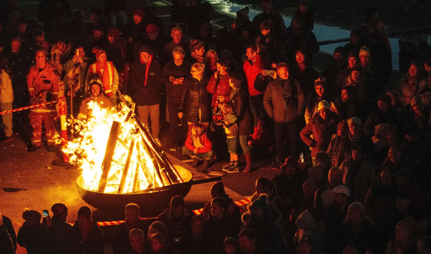 A crowd gathered around a blazing fire pit with fire safety personnel at the Big Sing Bonfire, Festival of Voices, Hobart