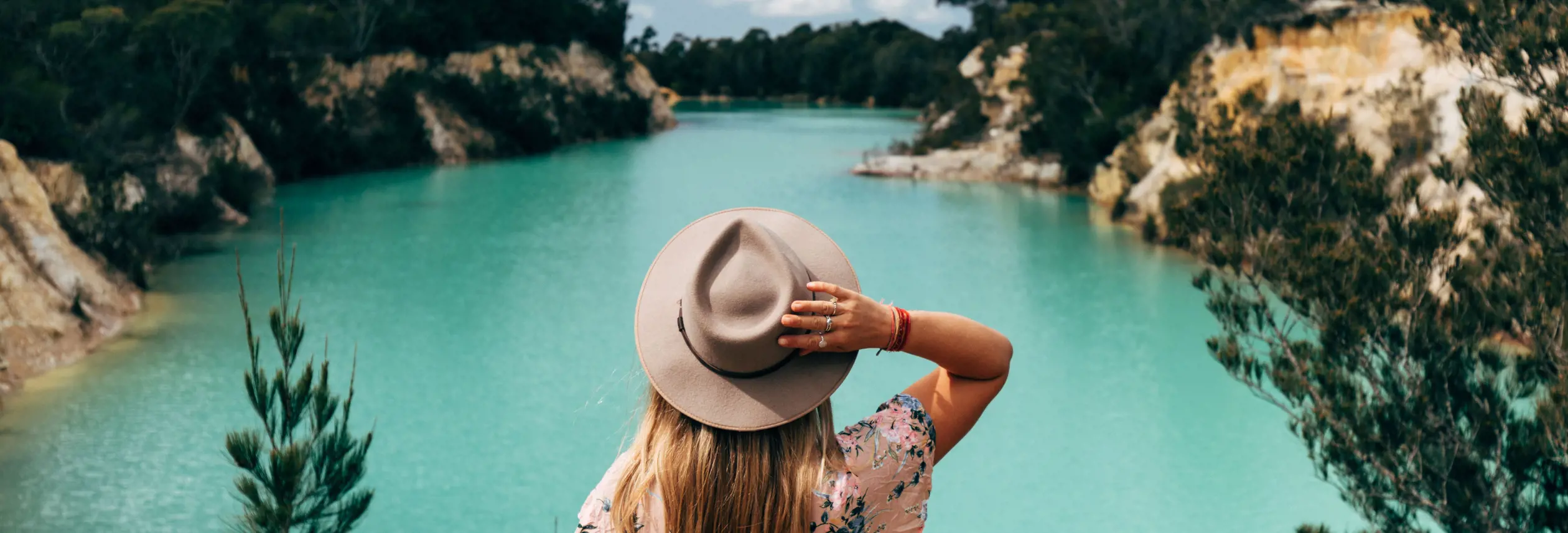 A person in a wide brim hat looking out over the turquoise water of Little Blue Lake near Poonerluttener / Mount Cameron