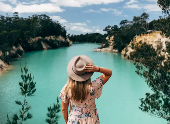 A person in a wide brim hat looking out over the turquoise water of Little Blue Lake near Poonerluttener / Mount Cameron