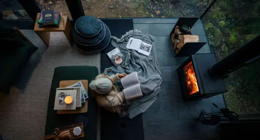 Overhead view of a person reading by a fireplace wrapped in a blanket with books and a candle at Pumphouse Point, Lake St Clair