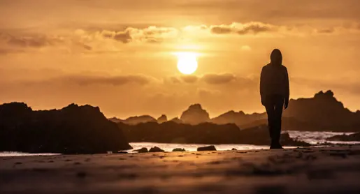 A person silhouetted on the beach at sunset with rocky outcrops at Arthur River, takayna / Tarkine