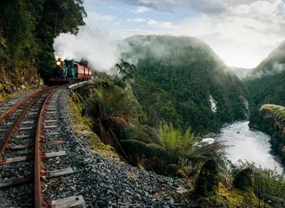 A West Coast Wilderness Railway steam train on the narrow mountain railway above a rainforest river gorge, Strahan