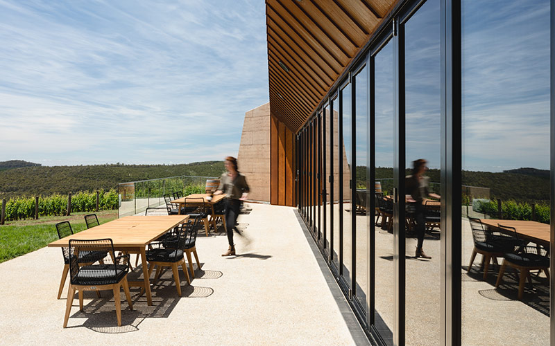 Outdoor furniture sits on a decking looks out over the green vines of a vineyard