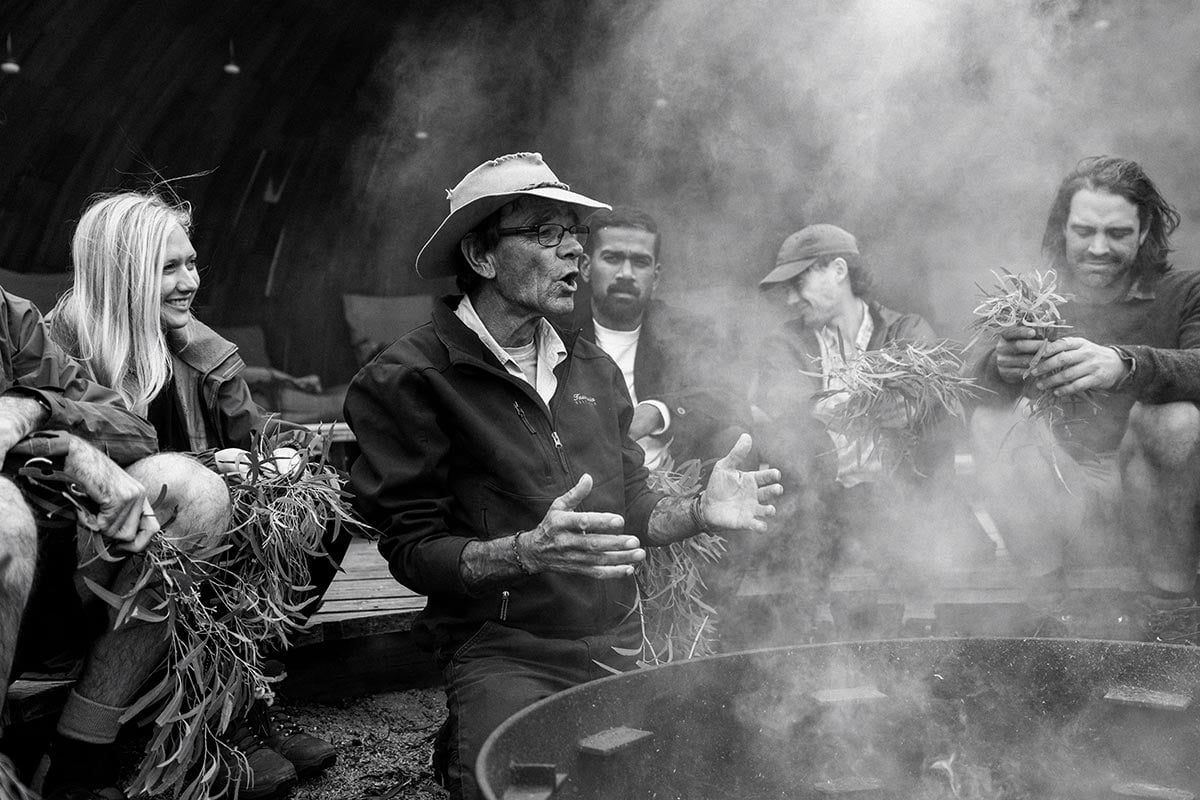 A man stands near a fire pit and talks to a group of people,