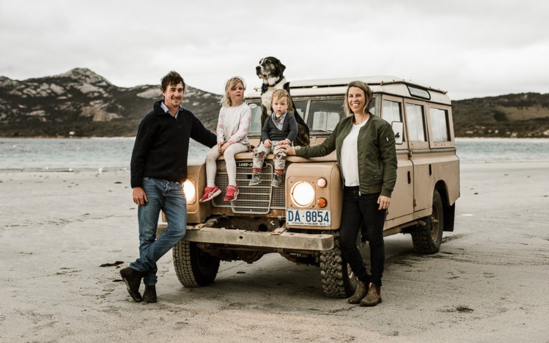 A family of four  stand on a beach on Flinders Island with their dog and their 4WD 