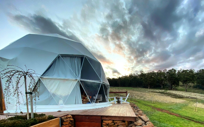 A large, white dodecahedron shaped tent with triangular windows stands in a field.