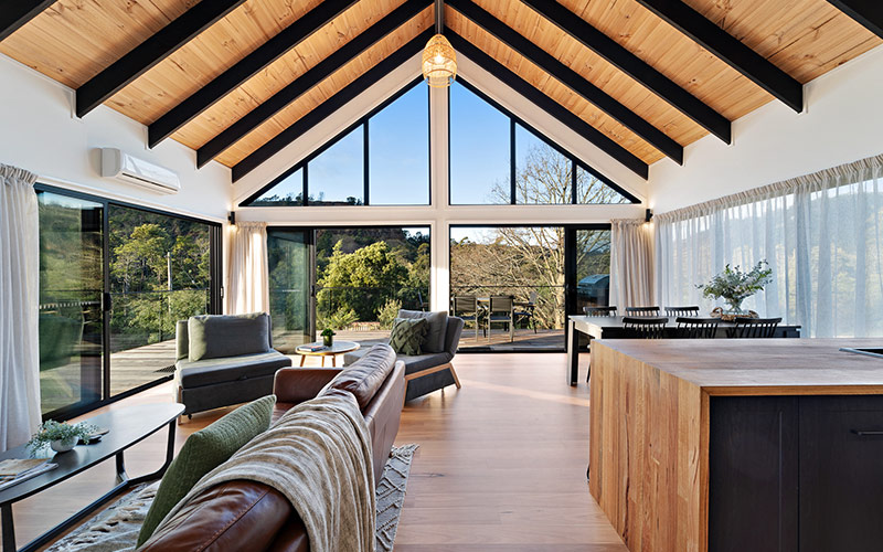 A photograph of the architectural interior of a modern cabin, with large floor to ceiling windows overlooking the forest