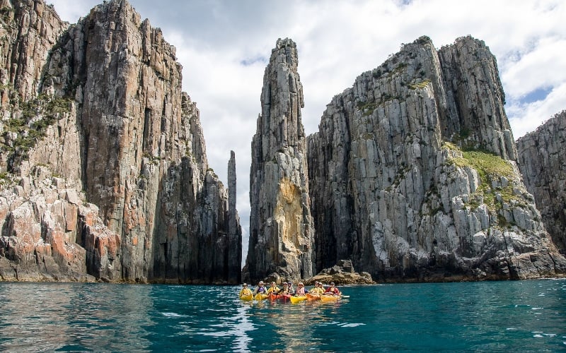 A group of kayakers pause in a group on the glass turquoise waters in front of the sea cliffs of the Tasman Peninsula 