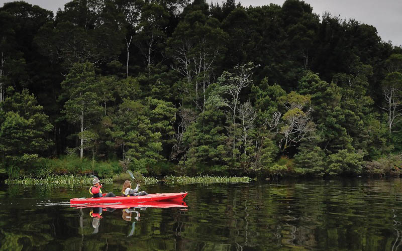 Two people in a canoe drift on river through the Tarkine wilderness