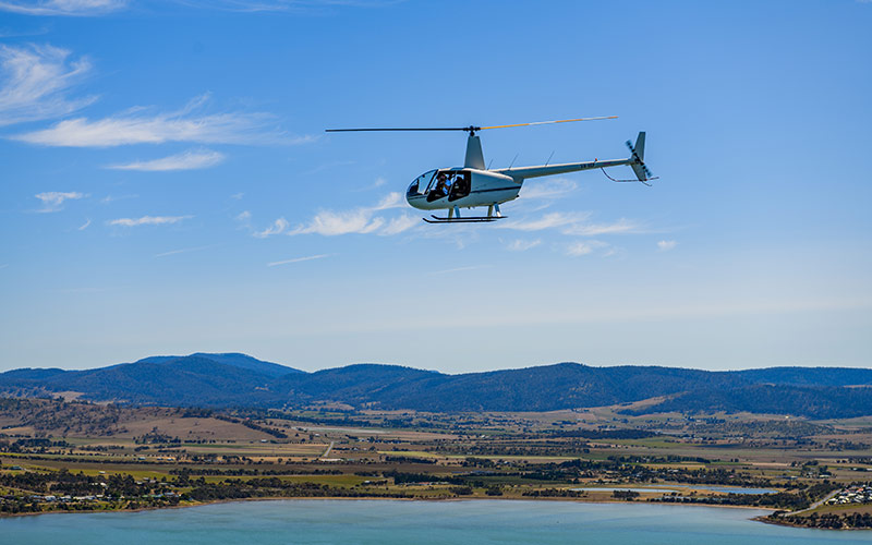 A light helicopter flies over a bay in southern Tasmania on a clear summer's day.