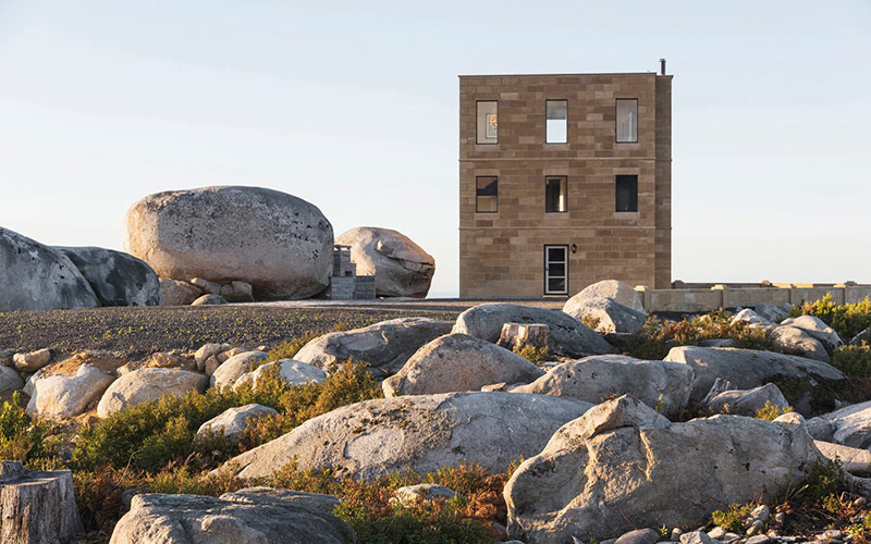 A modern tower built using colonial materials stands amongst granite boulders