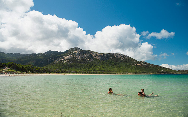 A young family bathe on the clear blue waters of Trousers Point, Flinders Island on a warm summer's day.