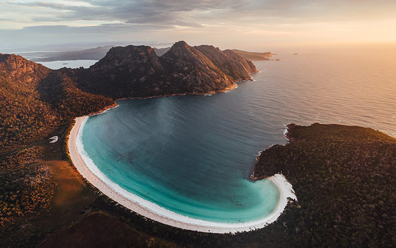 An aerial photograph of Wineglass Bay bathed in sunset light